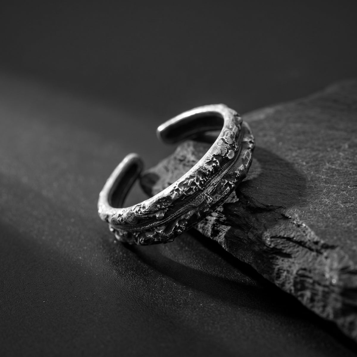 Angled close-up of the textured open band ring resting across a rough stone slab.