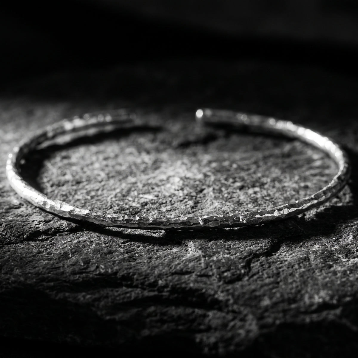 Low-angle close view of the hammered silver open cuff bracelet on textured dark stone.