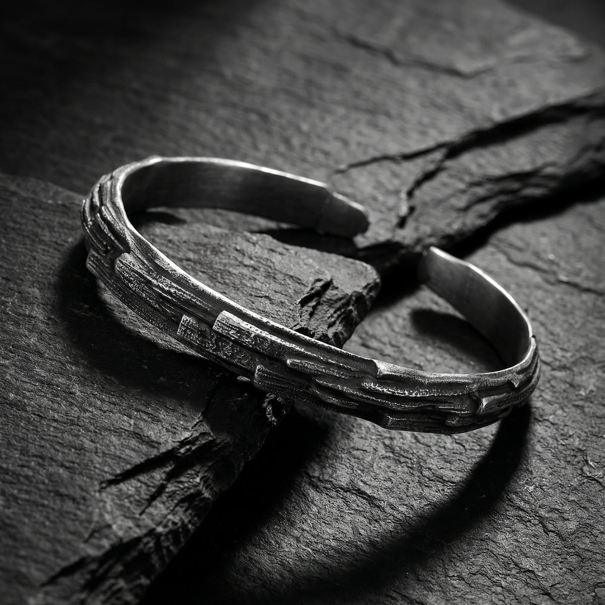 Angled view of the carved silver open cuff bracelet resting on a textured dark rock slab.