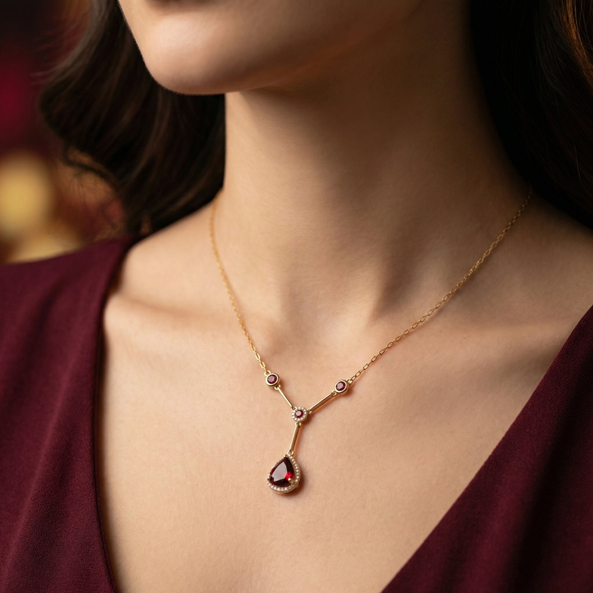 Model wearing the 18K yellow gold Persephone necklace with a pear cut natural garnet pendant.