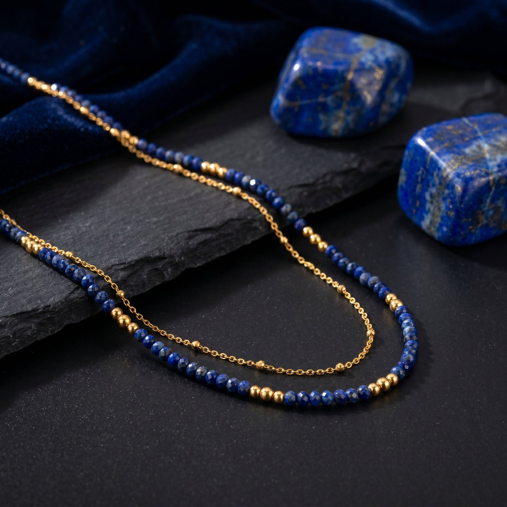 Macro view of faceted blue lapis beads and a gold-plated chain on a textured dark slate background.
