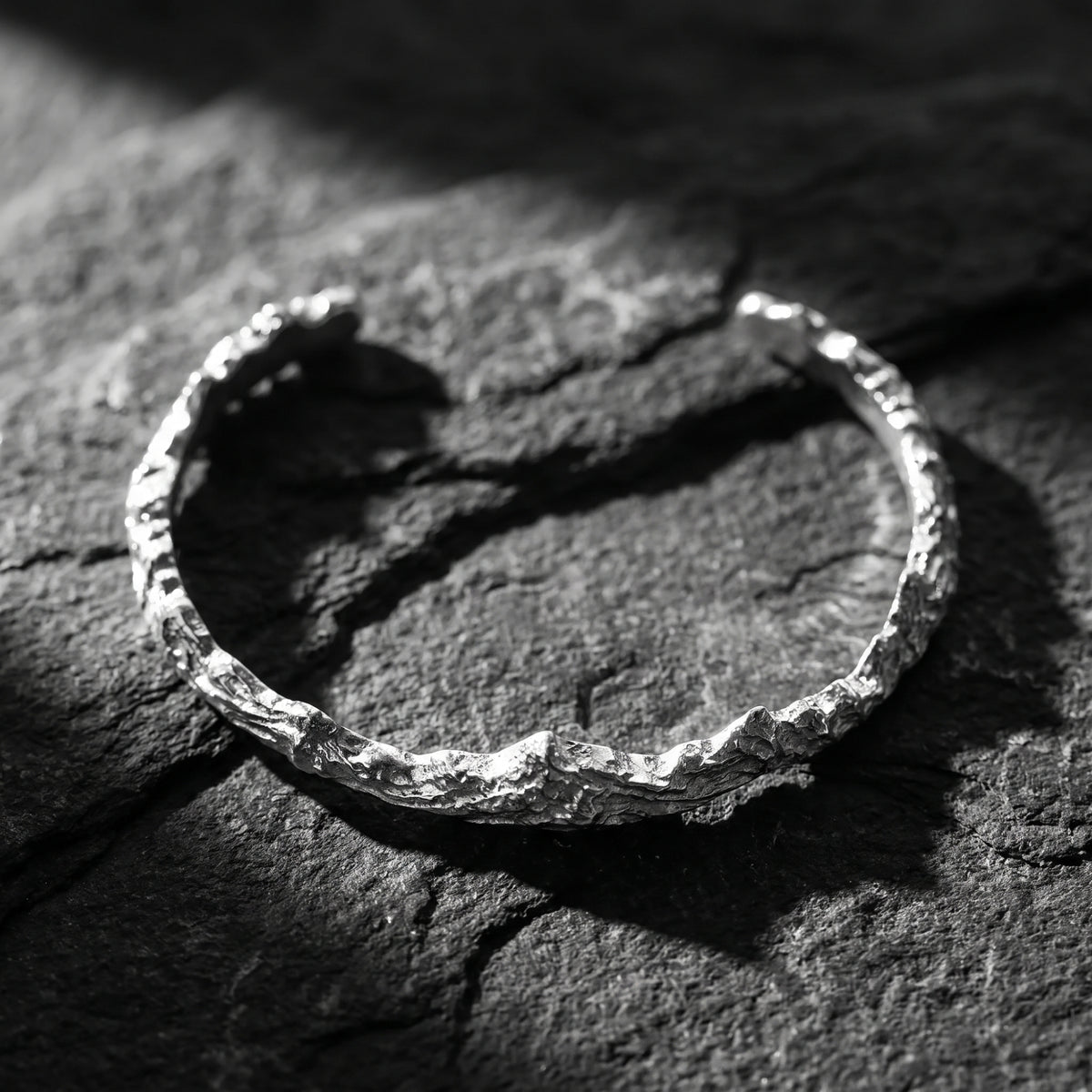 High-angle view of the textured silver mountain ridge open cuff bracelet resting on dark slate.