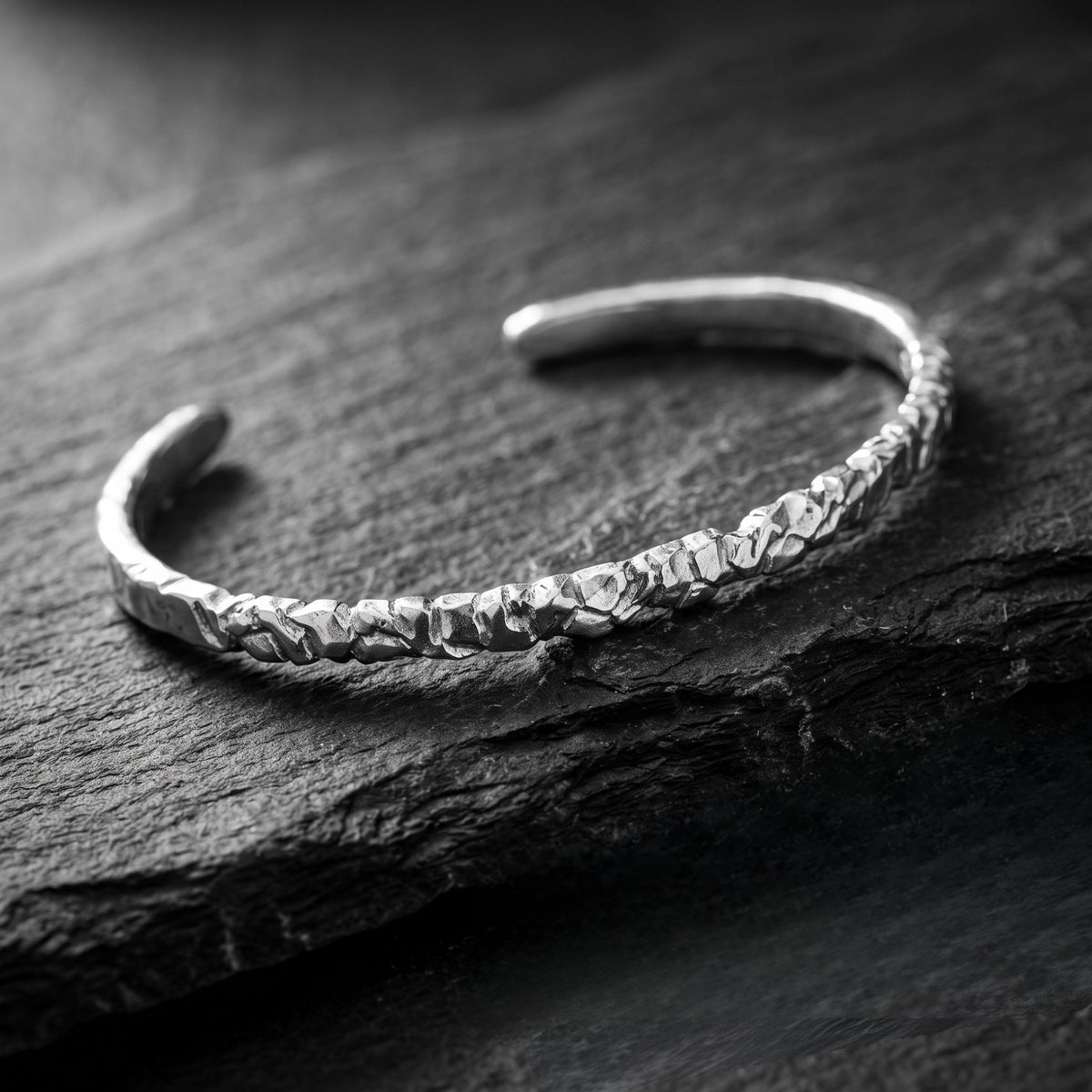 Angled close view of the textured silver open cuff bracelet resting on a dark slate surface.