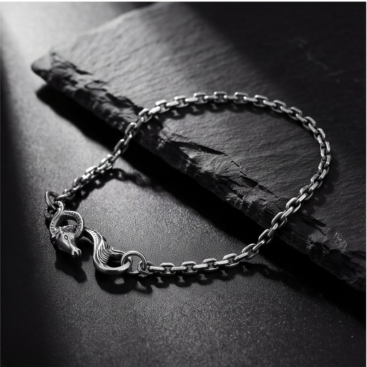 Angled view of the silver dragon chain bracelet on a dark surface, showing the sculpted dragon clasp.