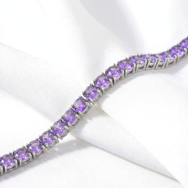 Close-up of round purple simulated amethysts in a stainless steel tennis bracelet setting on white fabric.