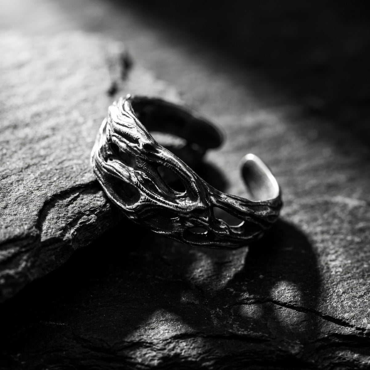 Angled view of the open silver ring with irregular textured openwork, displayed on a rough slate surface.