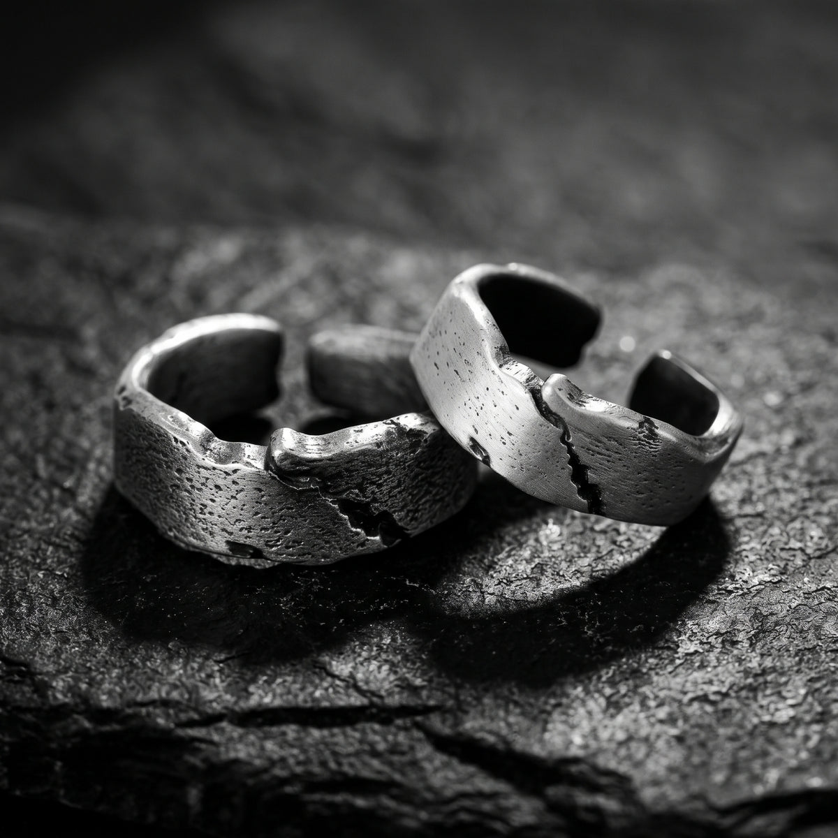 Two textured silver open rings overlap on a dark textured surface, showing their fissure details.