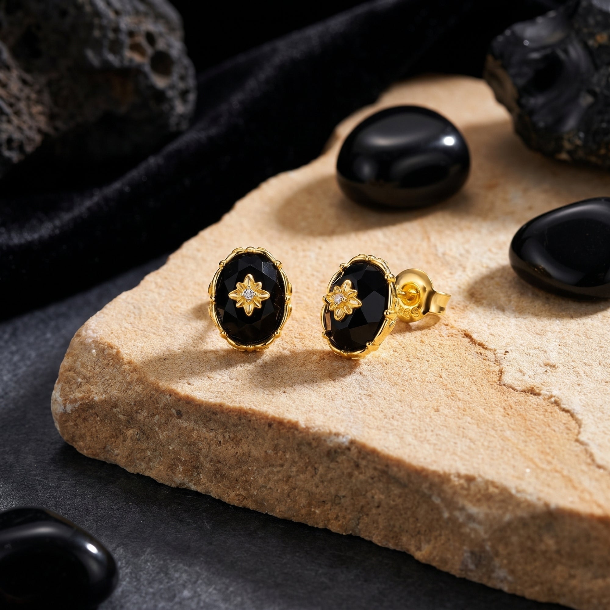 Close-up of yellow gold oval-cut faceted black onyx earrings showing the starburst detail and earring post.