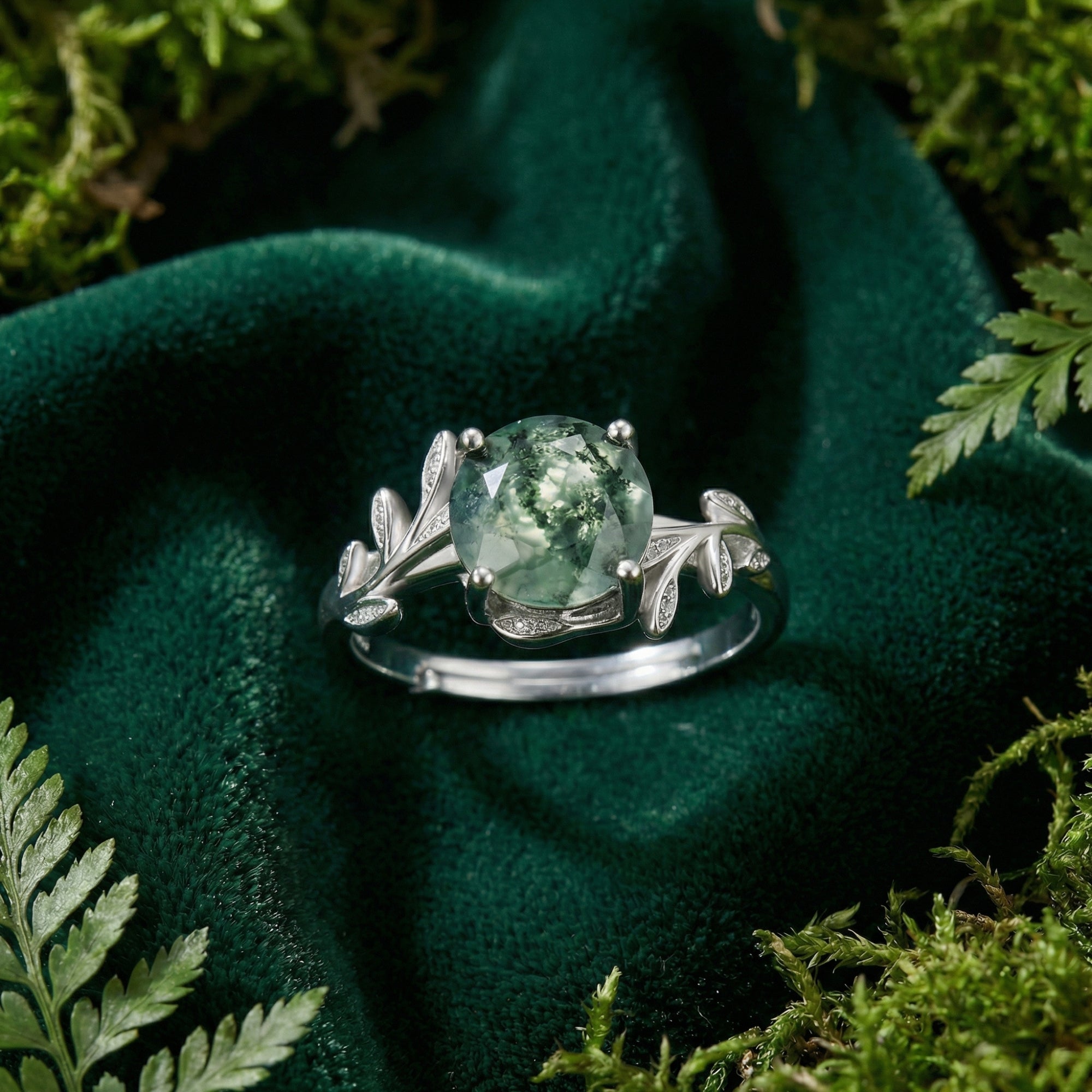Macro top-down view of a silver S925 moss agate ring with leaf details on a dark green velvet background.