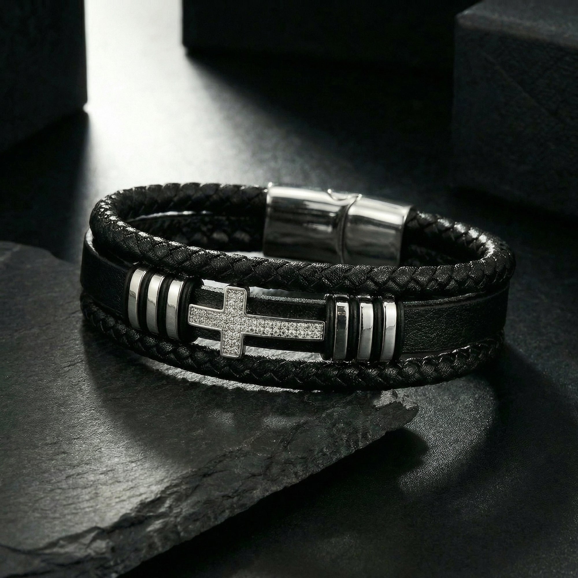 Close-up of the Aegis Cross Bracelet showing the stainless steel cross with pavé stones and braided leather.