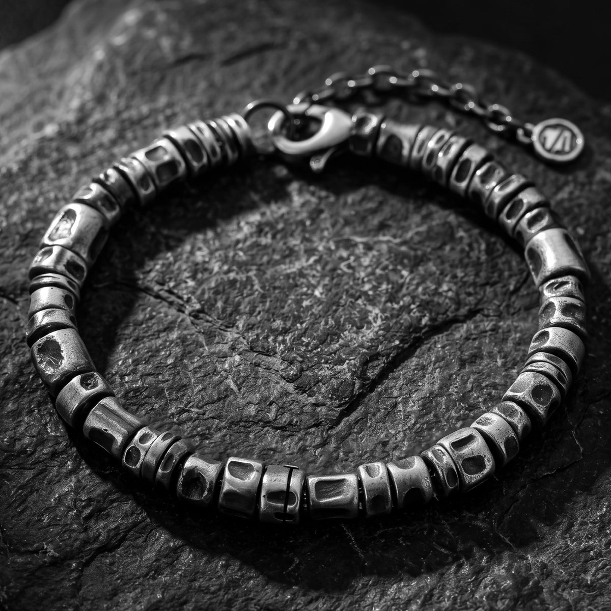 Close-up view of the textured silver barrel-link bracelet with its lobster clasp on a dark slate surface.