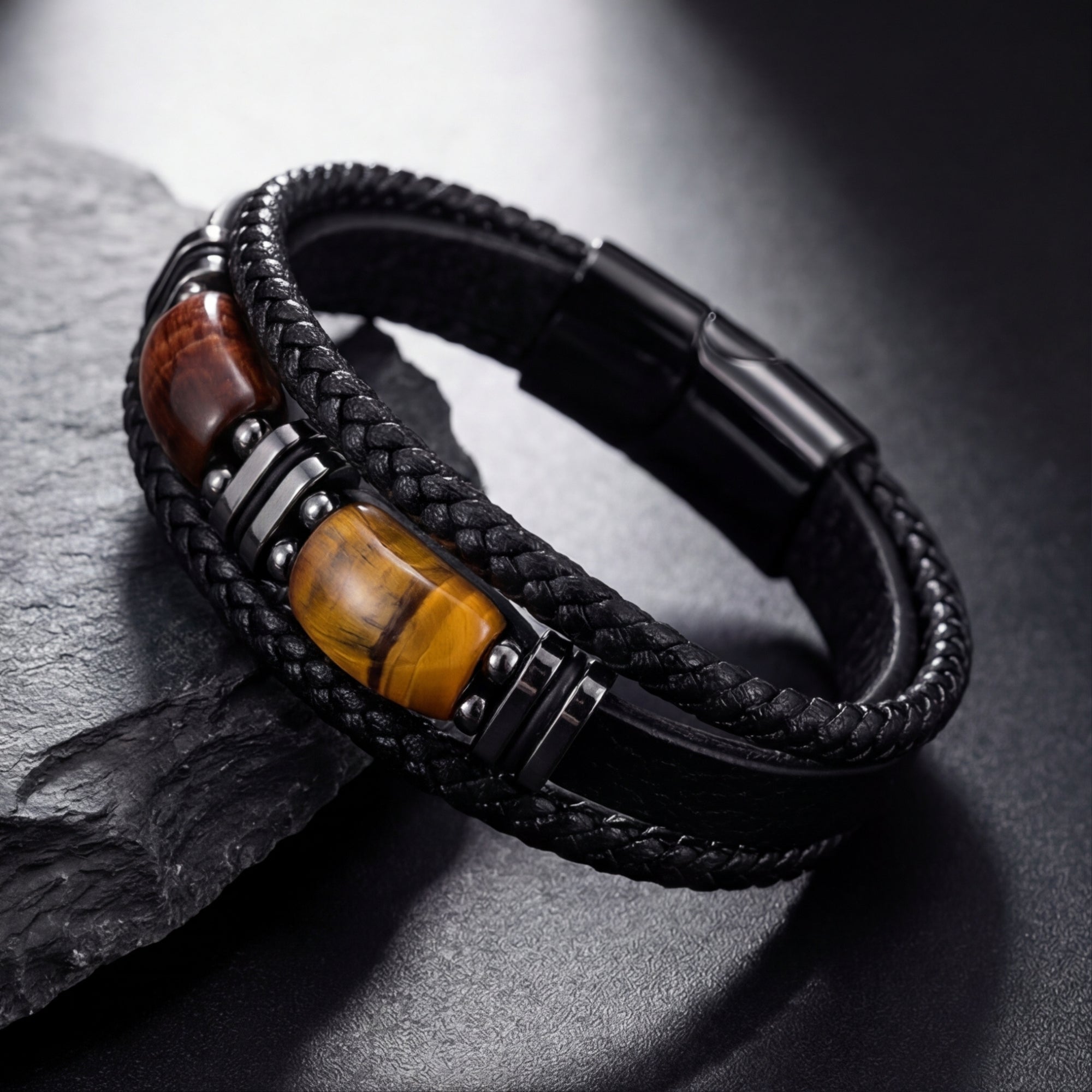 Close-up of a black braided leather bracelet featuring red and yellow tiger's eye barrel beads and black steel spacers.