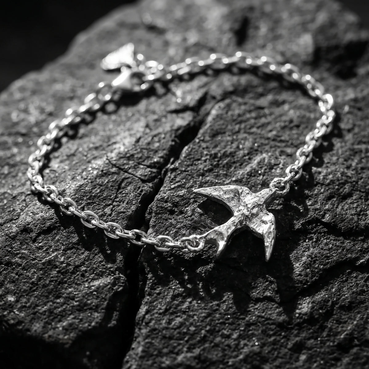 Top-down view of the silver swallow chain bracelet on cracked dark stone, with its clasp visible.
