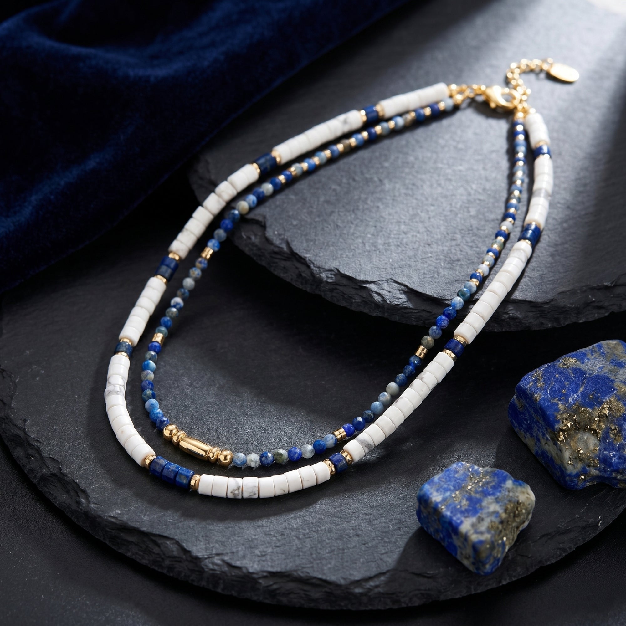 Two-strand gold-plated necklace set featuring natural lapis lazuli and white beads displayed on dark slate.