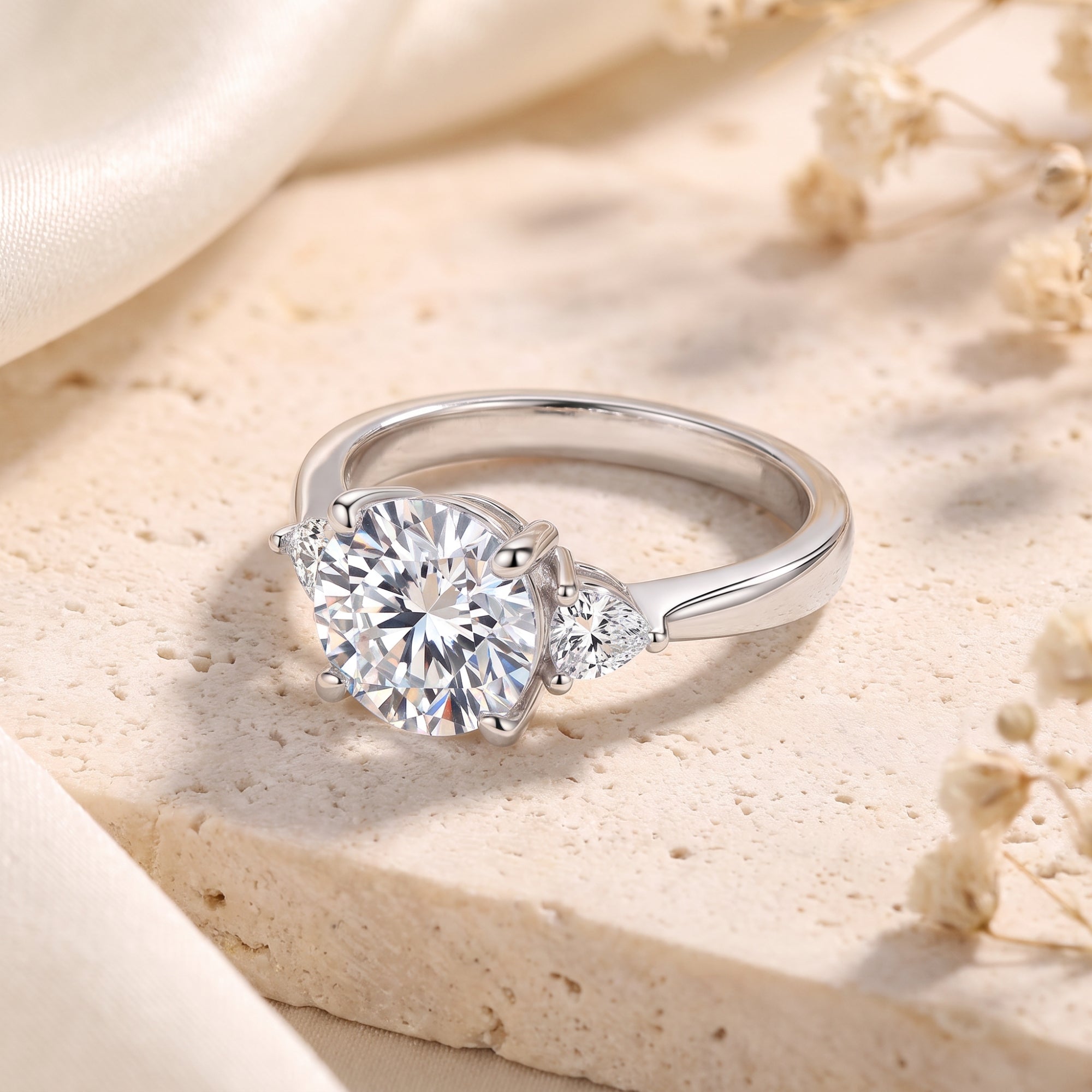 Angled view of silver trilogy ring with round and pear-cut stones.