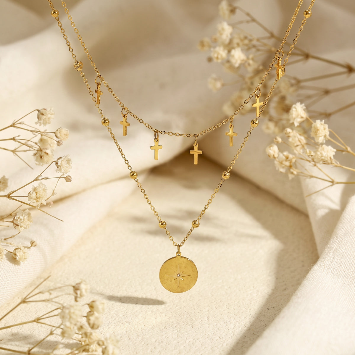 Symmetrical display of a gold-tone layered necklace with cross charms and a round star pendant on cream fabric.