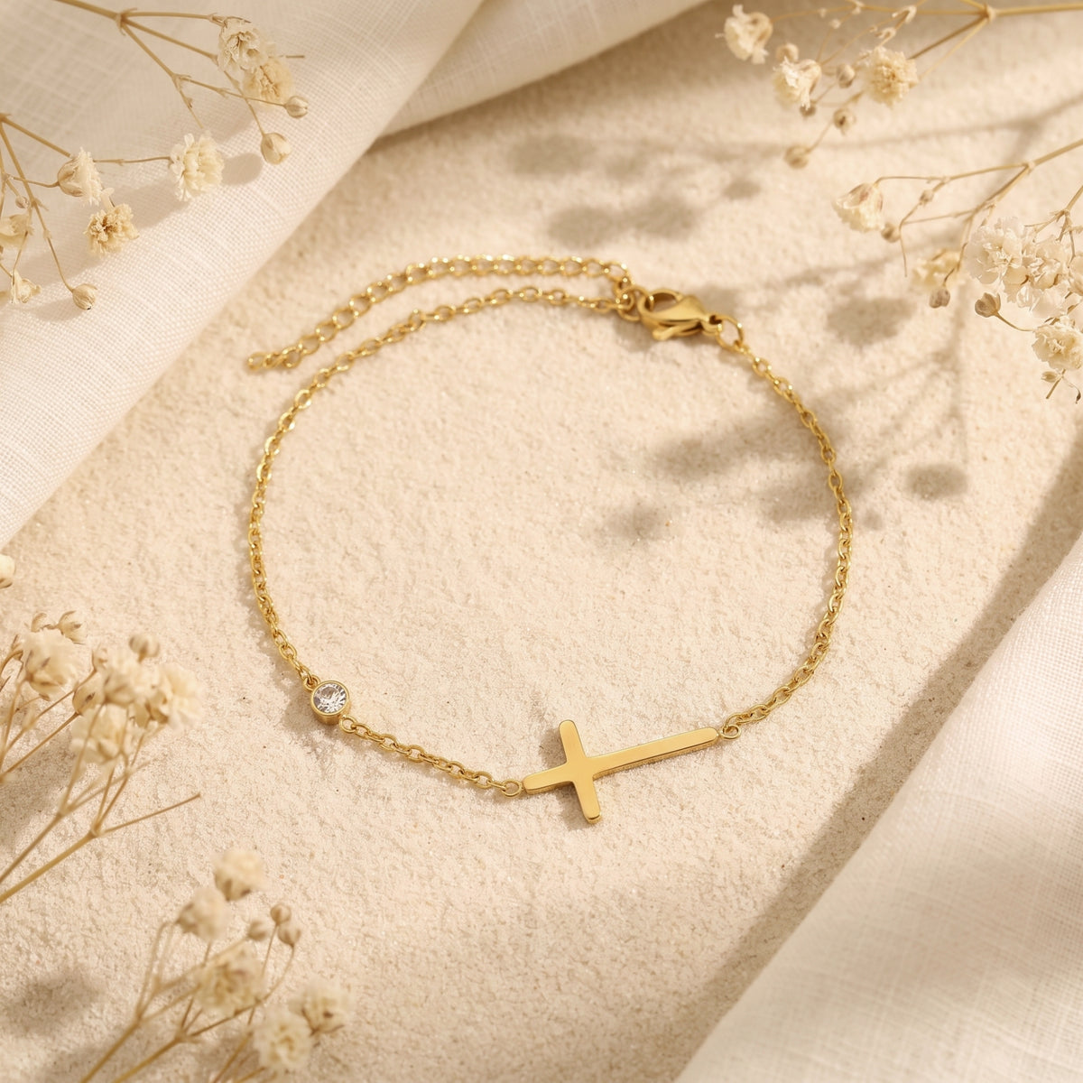Top-down view of the gold-tone sideways cross bracelet with cubic zirconia, lobster clasp, and extender chain visible.
