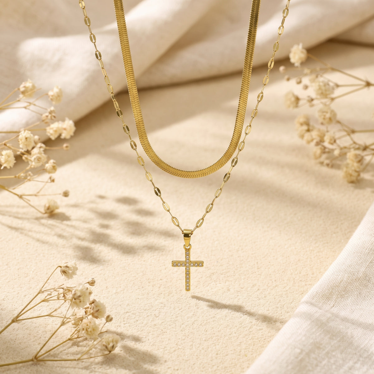 Hanging view of the gold-tone layered necklace showing the upper herringbone chain and lower pavé cross pendant.