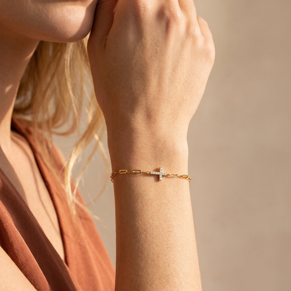 Close-up of a gold-tone paperclip bracelet with a pave-set cross worn on a wrist.