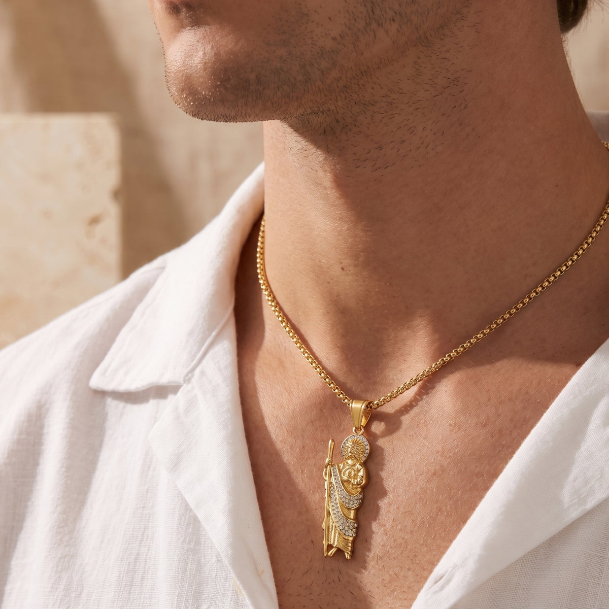 Side-angle view of a model wearing a gold-tone St. Jude pendant necklace with a white linen shirt.