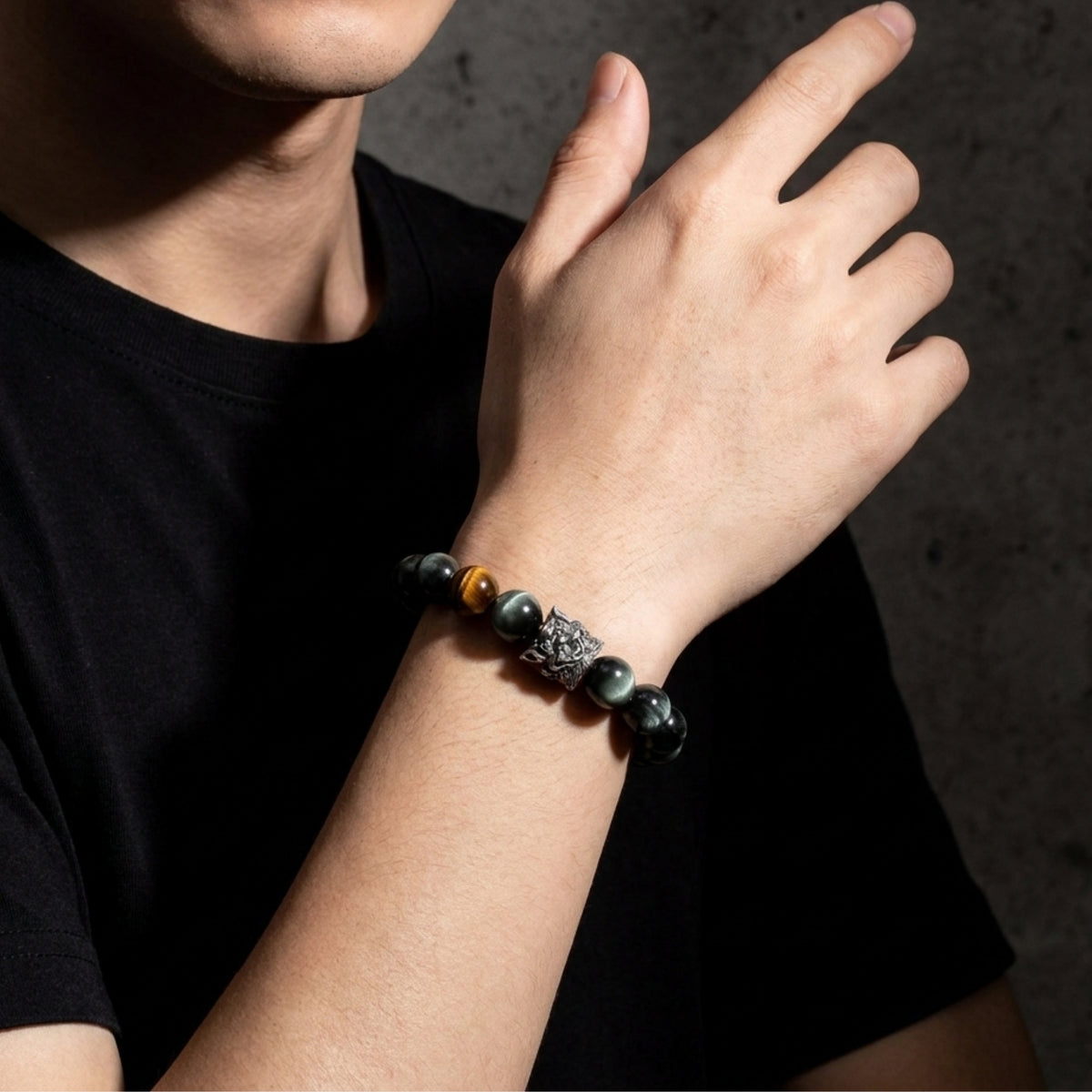 Dark stone beaded bracelet with a silver lion charm worn on a person's wrist with an open hand raised.