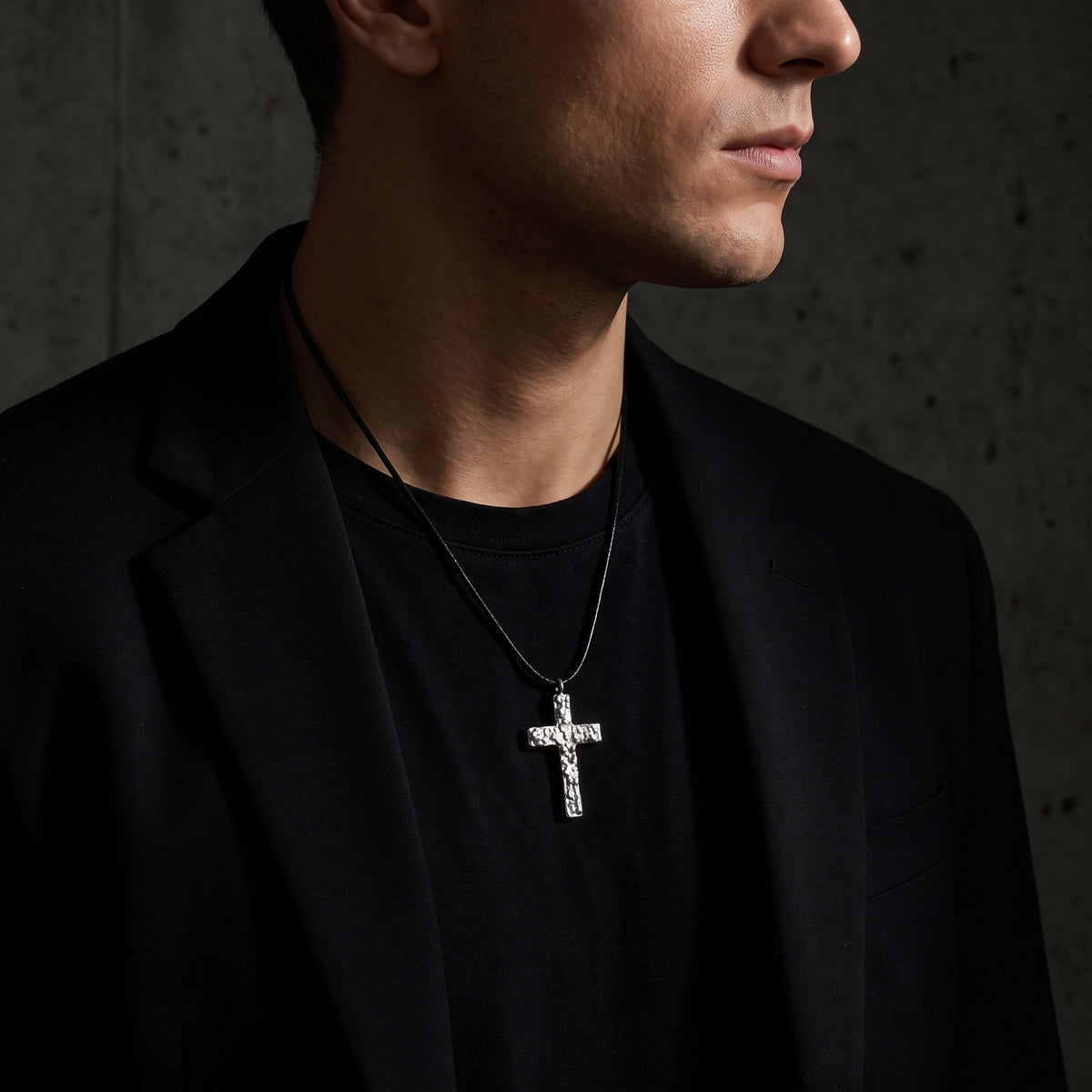 Model wearing a textured silver cross pendant on a black cord over a black shirt and blazer.
