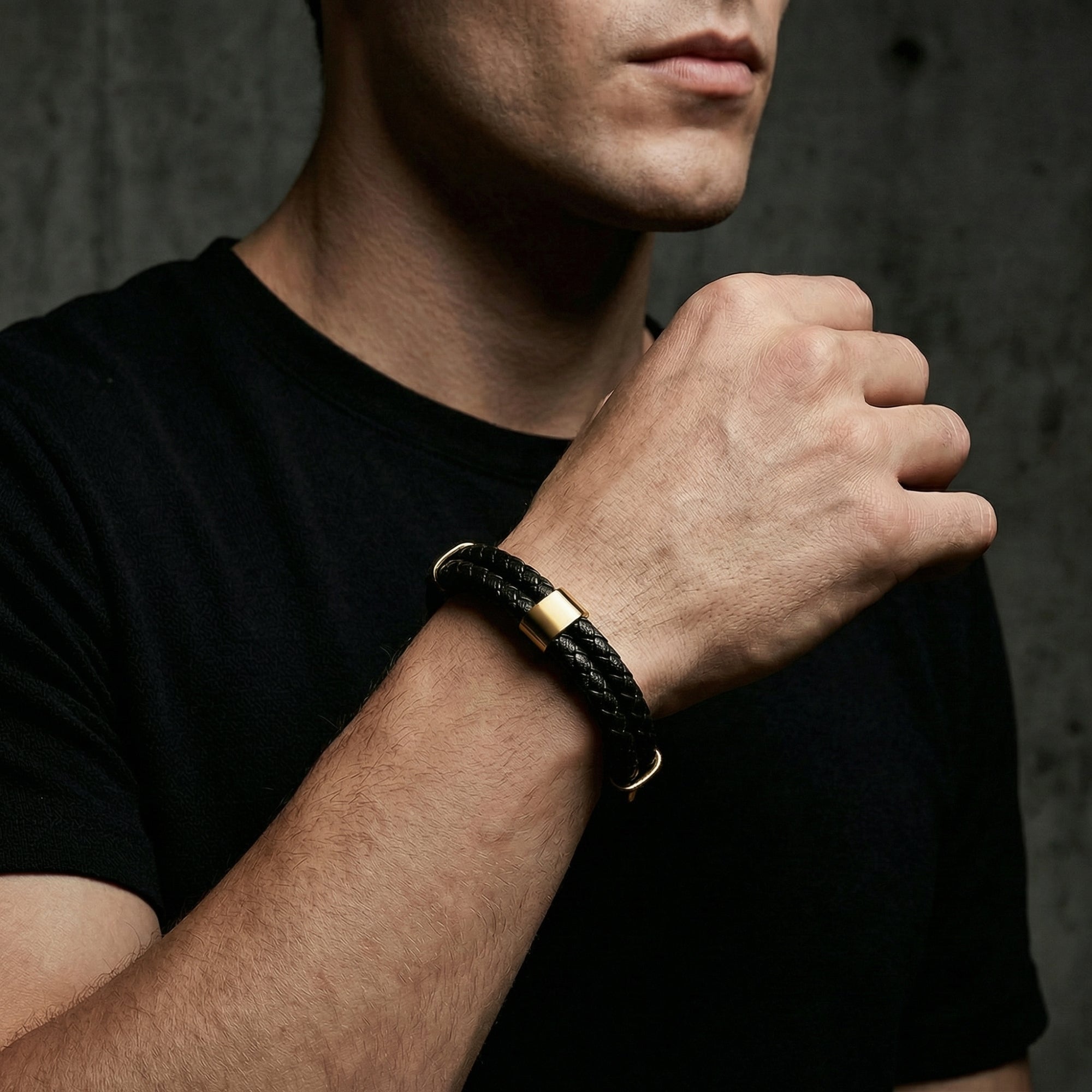 Men's black braided leather bracelet with gold steel accents styled on a wrist with a black shirt.