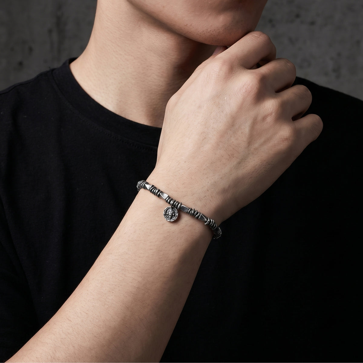 Man wearing the silver textured bracelet on his wrist with his hand resting near his chin.