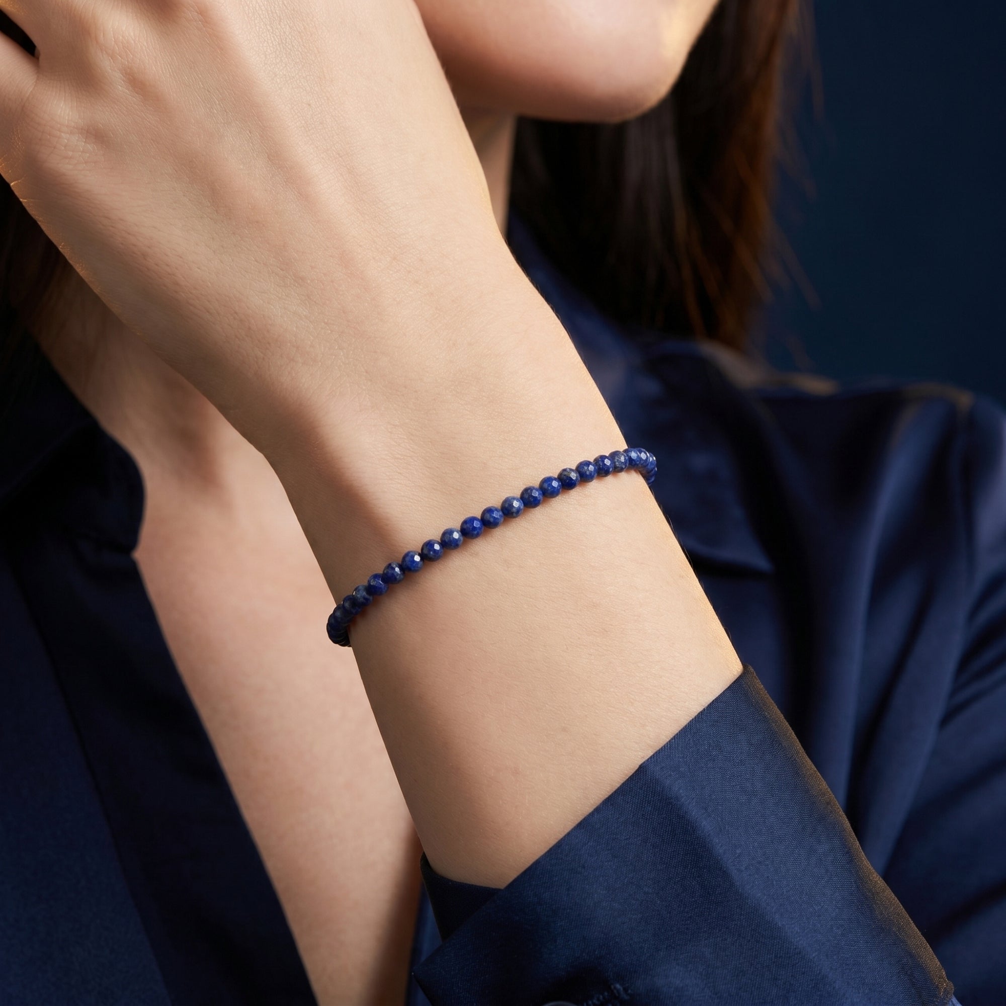 Macro shot of faceted lapis lazuli beads on a gold bracelet worn on a woman's wrist.