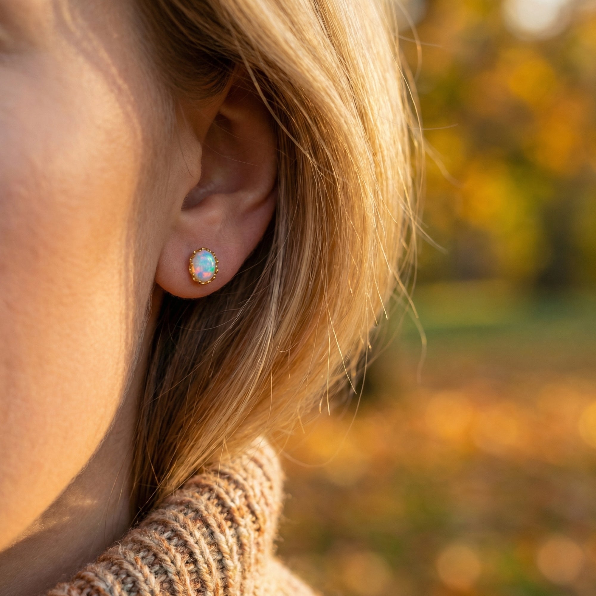 Close-up of a yellow gold Novalie stud earring with an oval white opal worn on a woman's ear.