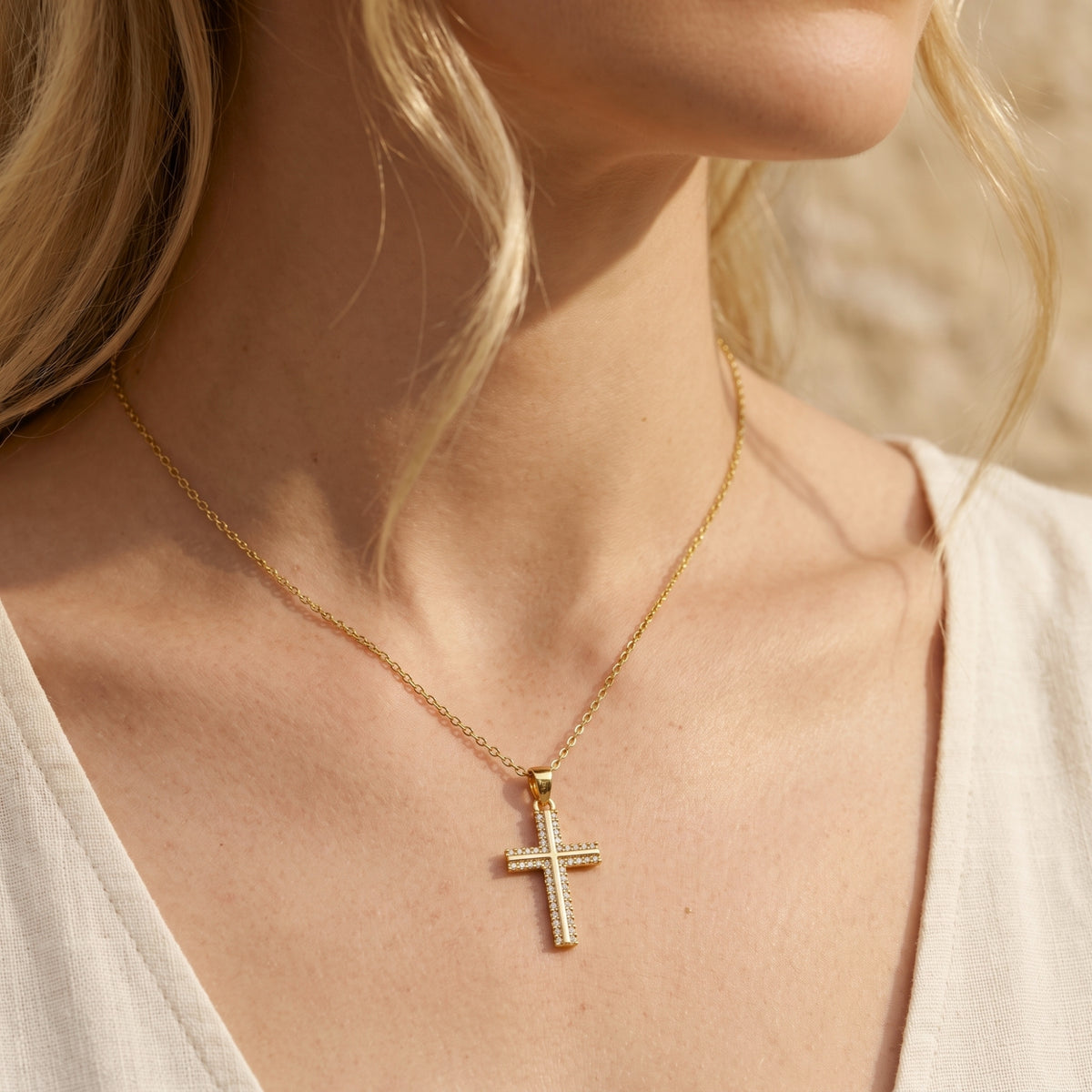 Model wearing a gold-tone dual-bar pavé cross necklace with a cream V-neck top.