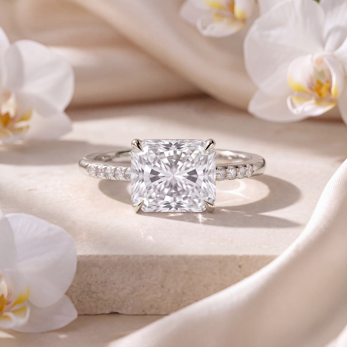 White gold radiant cut moissanite engagement ring with a pavé band displayed on a stone surface.