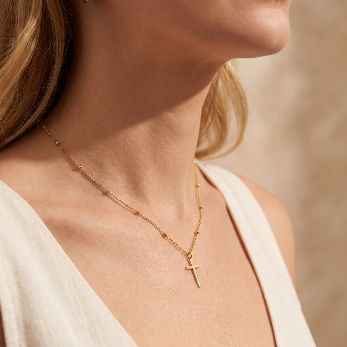 Side-angle view of a model wearing the gold-tone station cross necklace with a sleeveless cream top.