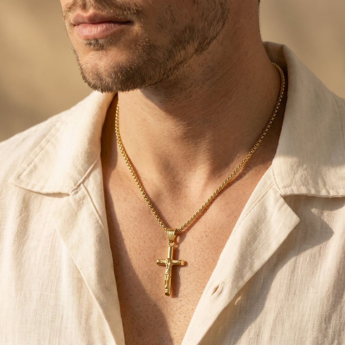 Man wearing a gold-tone crucifix pendant necklace with an open-collar cream shirt.