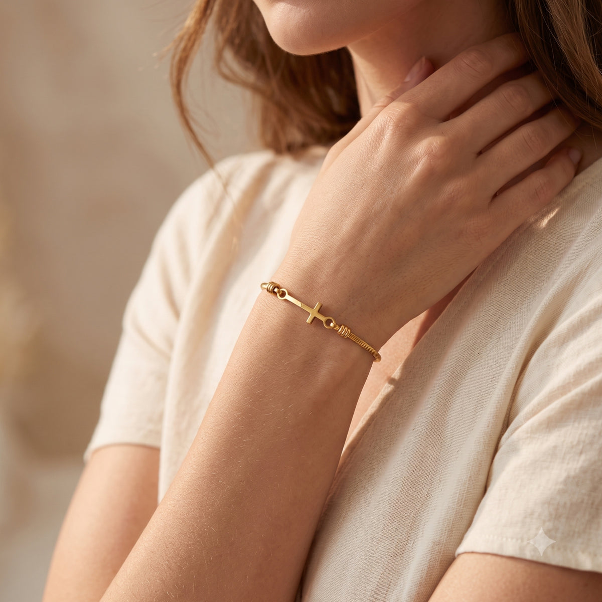 Model wearing the gold-tone twisted cross bracelet on her wrist with a light cream short-sleeved top.