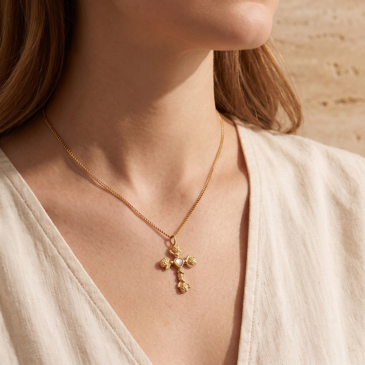 Close-up of a model wearing the gold-tone rose cross necklace over a light-colored open-neck top.