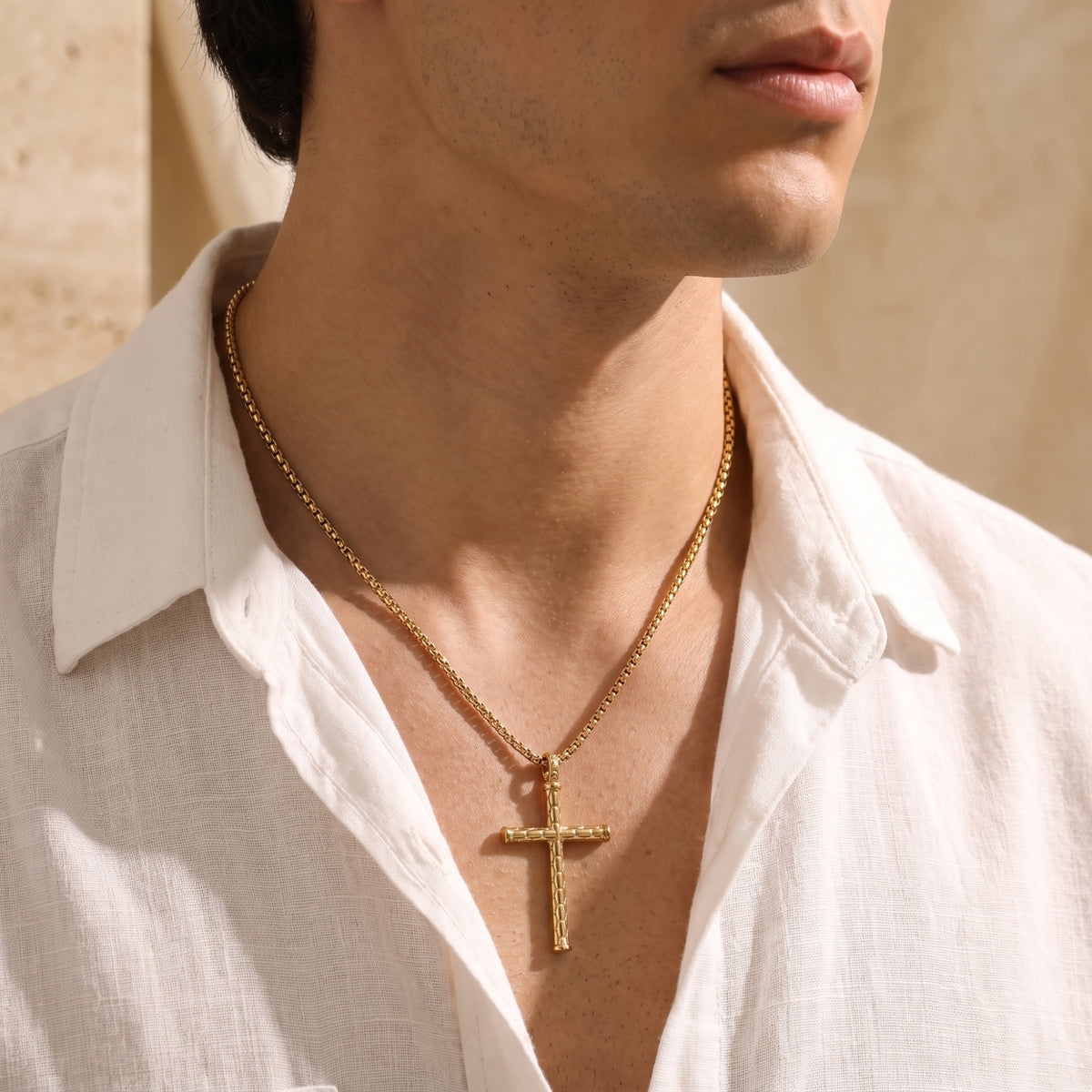 Close-up side view of a man wearing a gold-tone segmented cross necklace with an open white shirt.