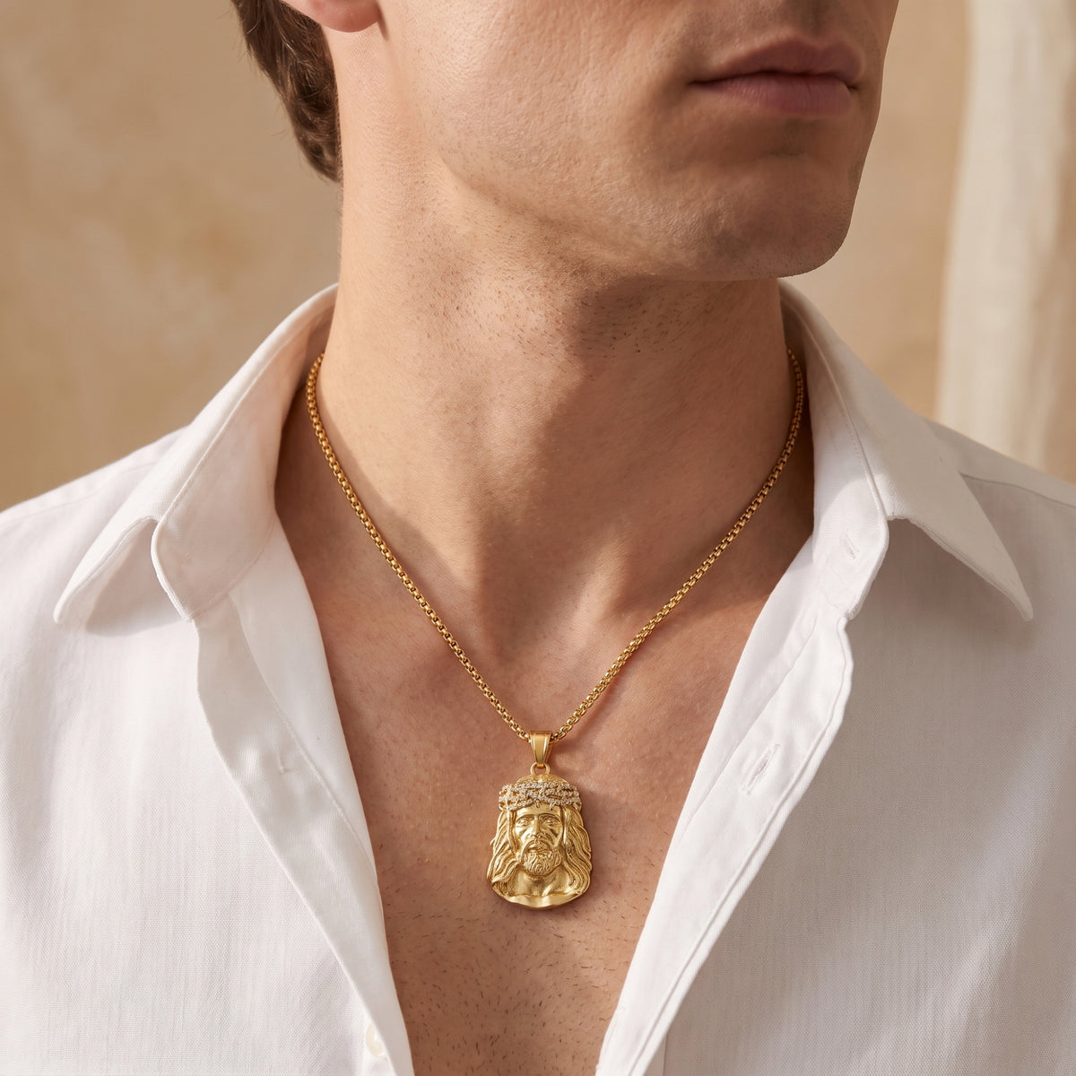 Front view of a man wearing a gold-tone Jesus portrait pendant with an open white shirt.