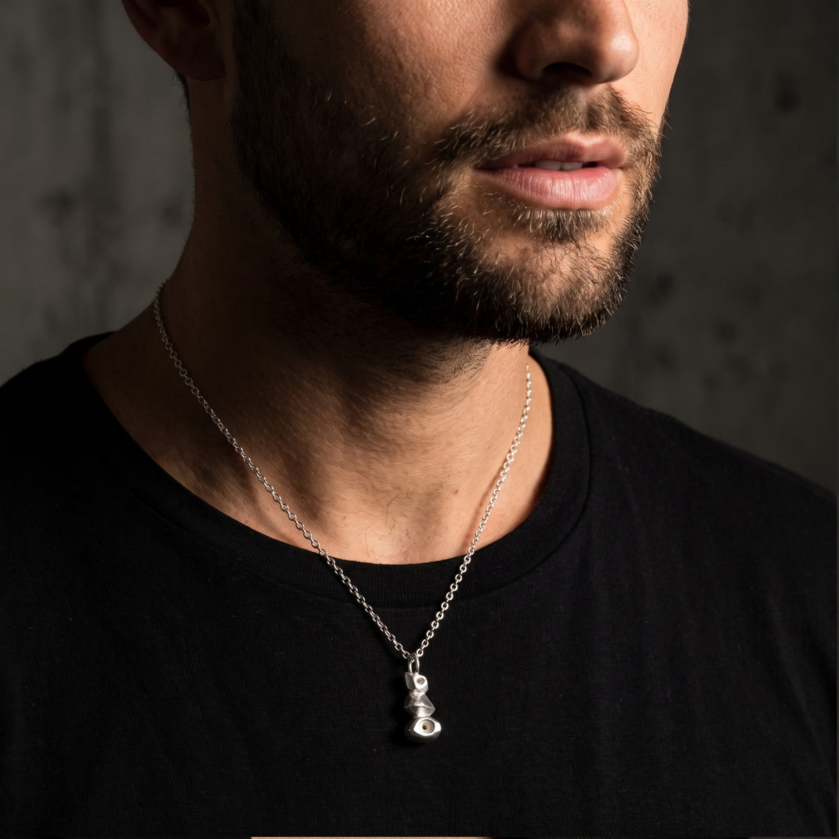 Close-up of a bearded man wearing the silver cairn pendant necklace over a black T-shirt.