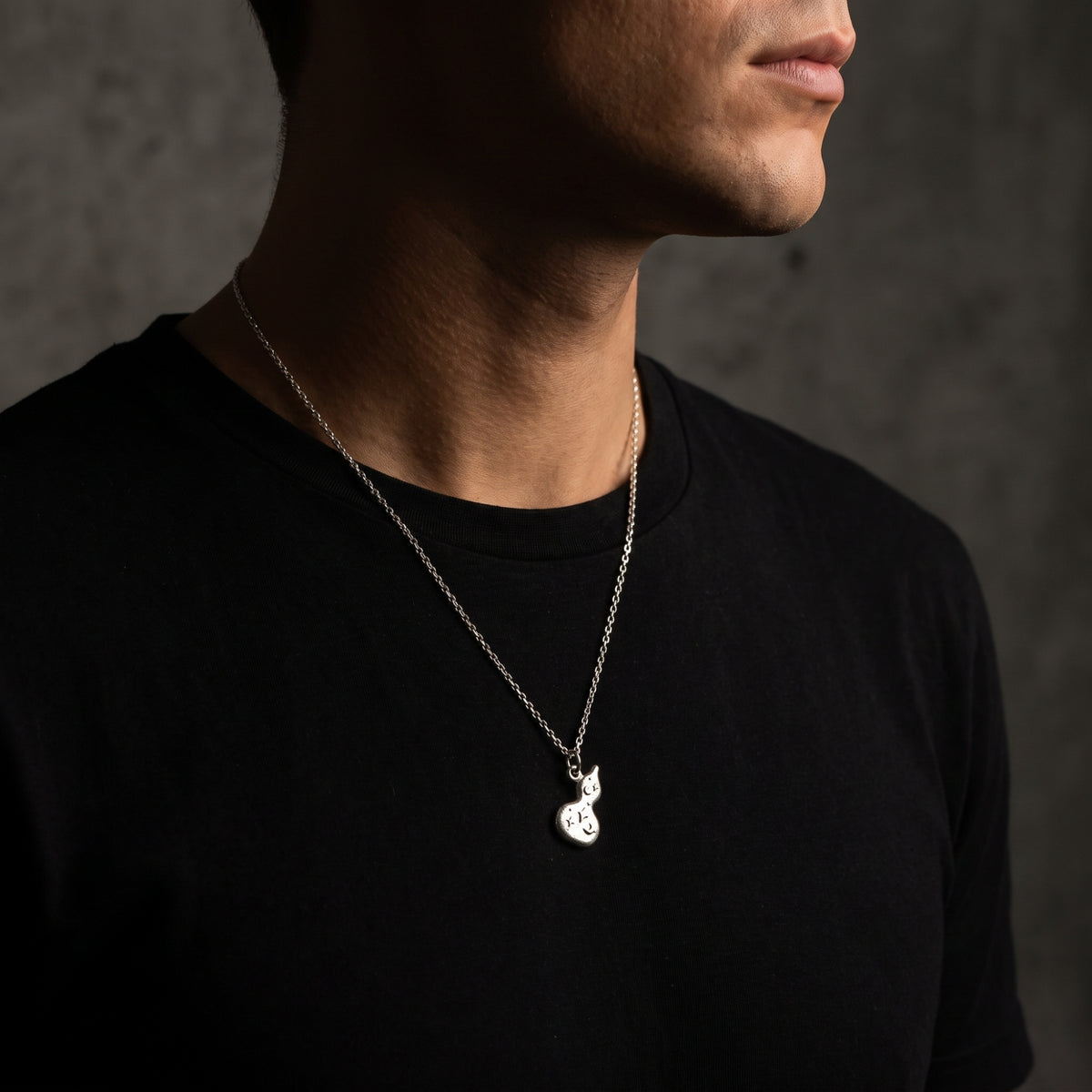 Three-quarter view of a man wearing the silver gourd pendant necklace over a black shirt.