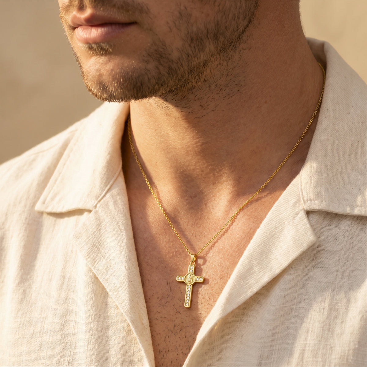 Gold-tone cross pendant necklace worn with clear stone accents over an open-collar white linen shirt.