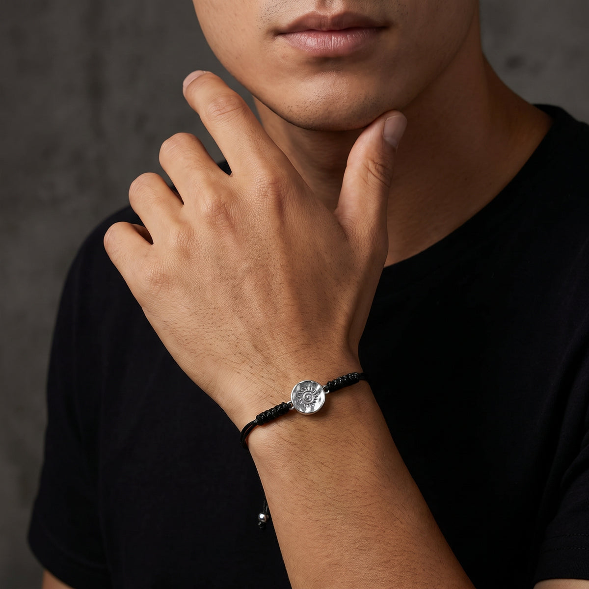 Close-up of a man wearing the black cord sun medallion bracelet with his hand raised to his chin.