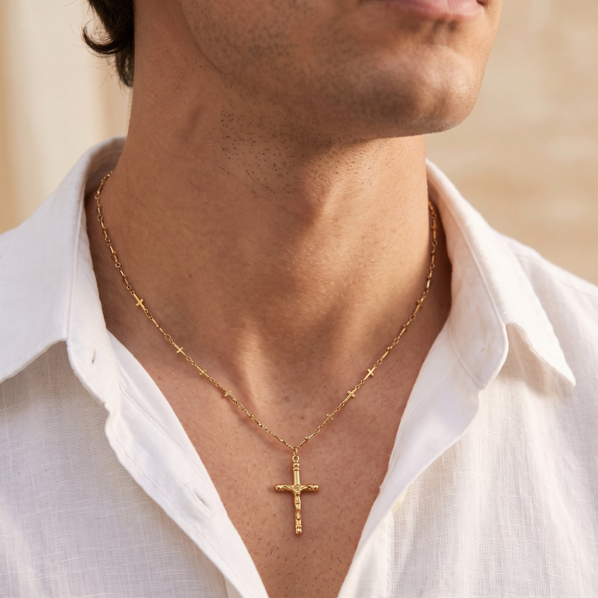 Front close-up of a man wearing the gold-tone station crucifix necklace over a white shirt.
