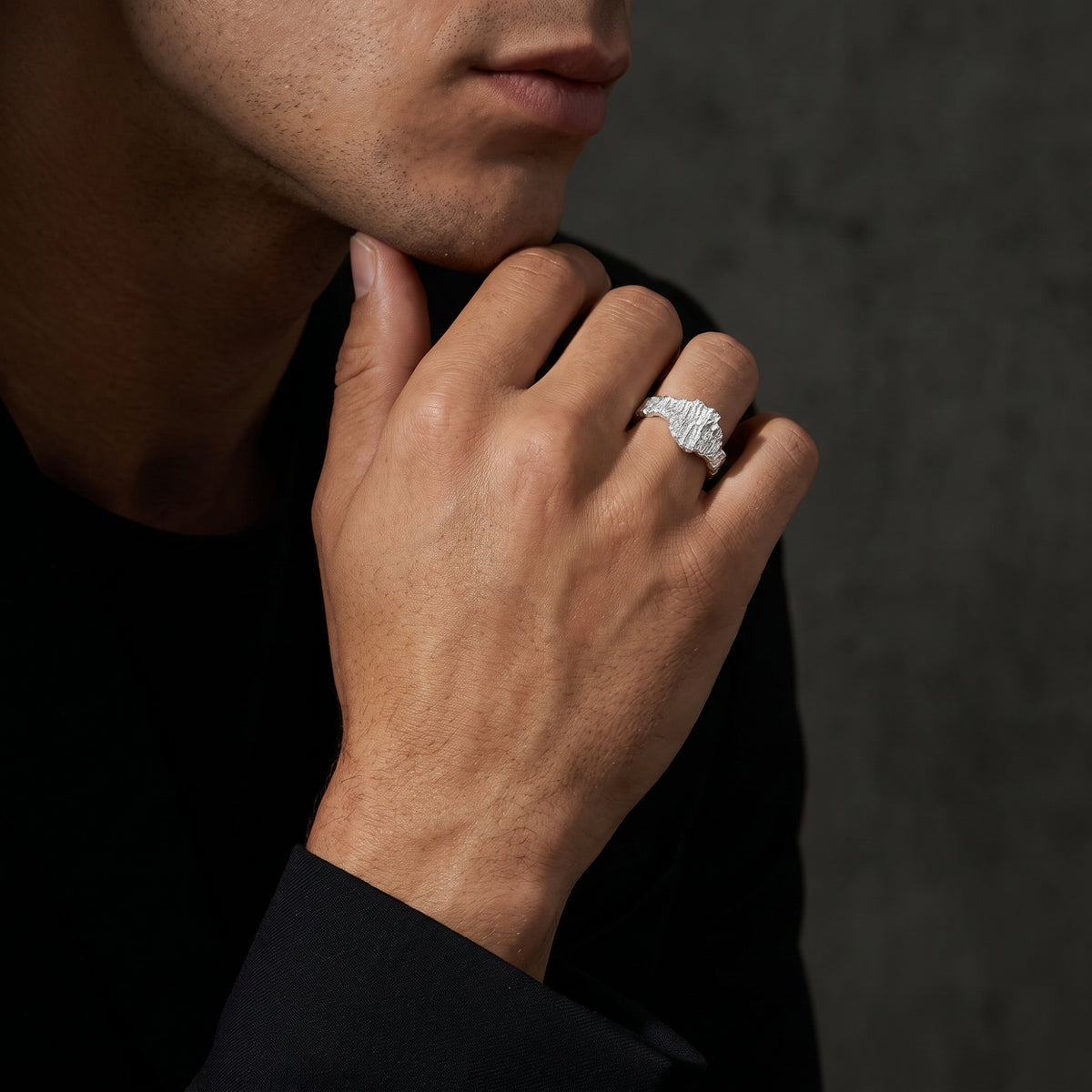 Close-up of a man wearing the sculpted silver bark ring on his ring finger against a black shirt.