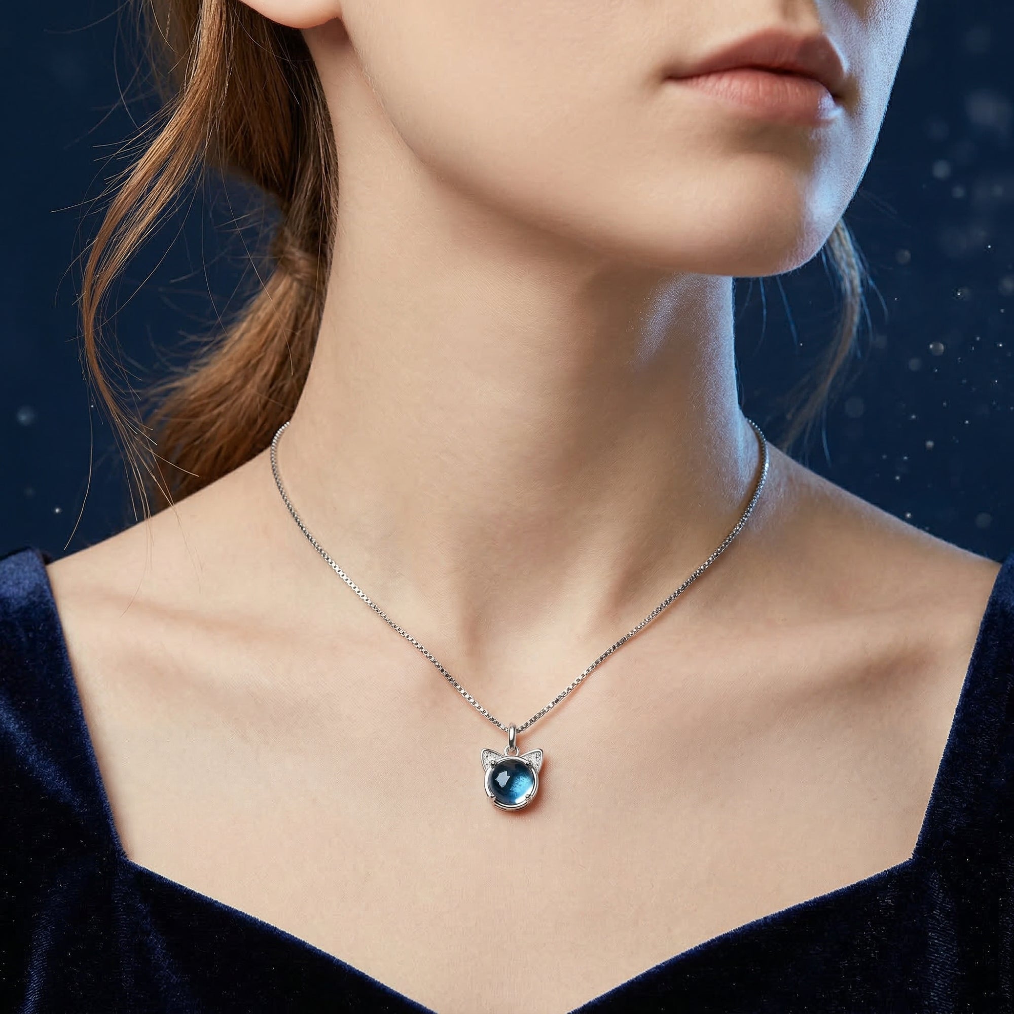A model wearing the silver Swiss Blue topaz cat pendant necklace against a dark blue backdrop.