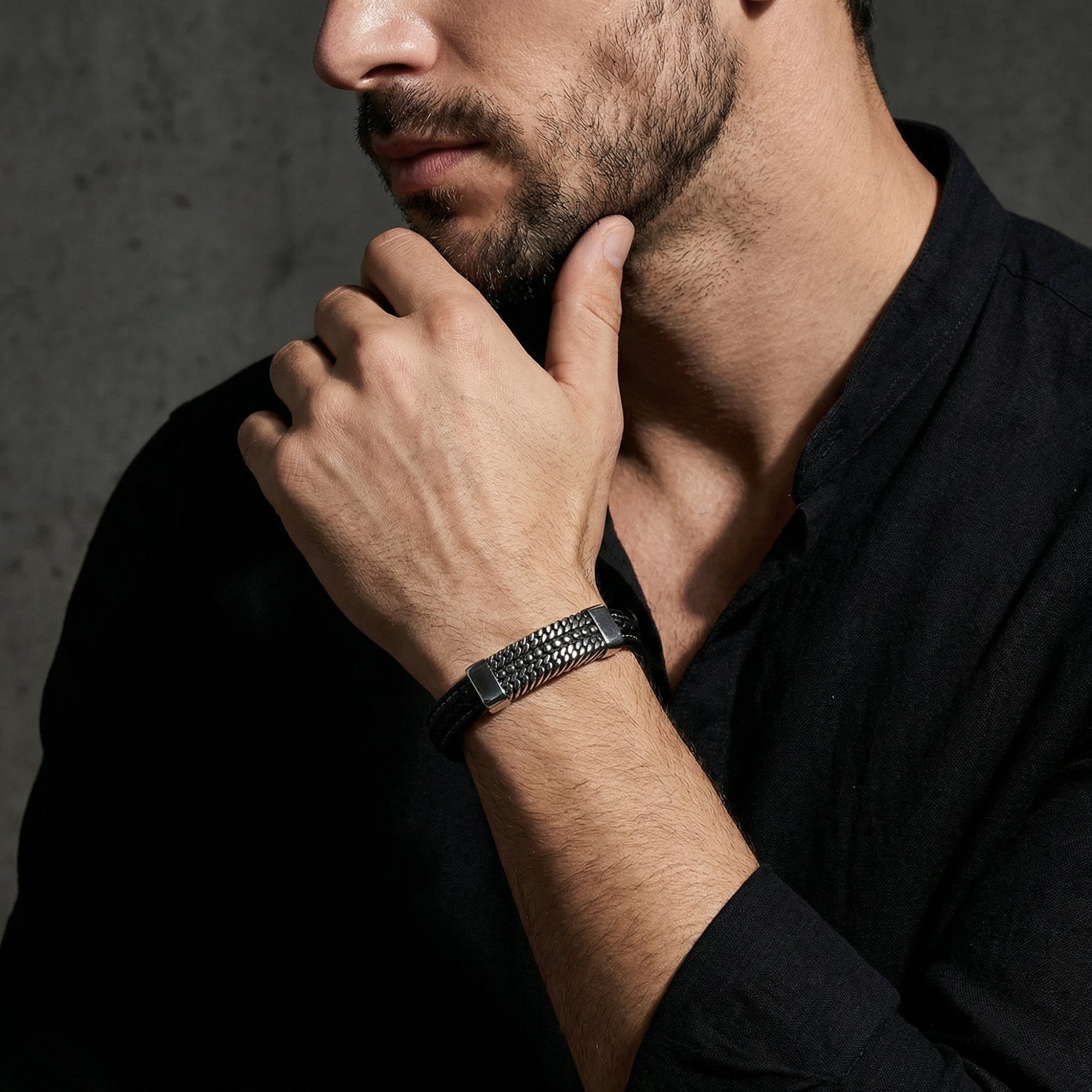 The Kinetic Bracelet with black braided leather and a silver stainless steel plate worn by a man in a black shirt.