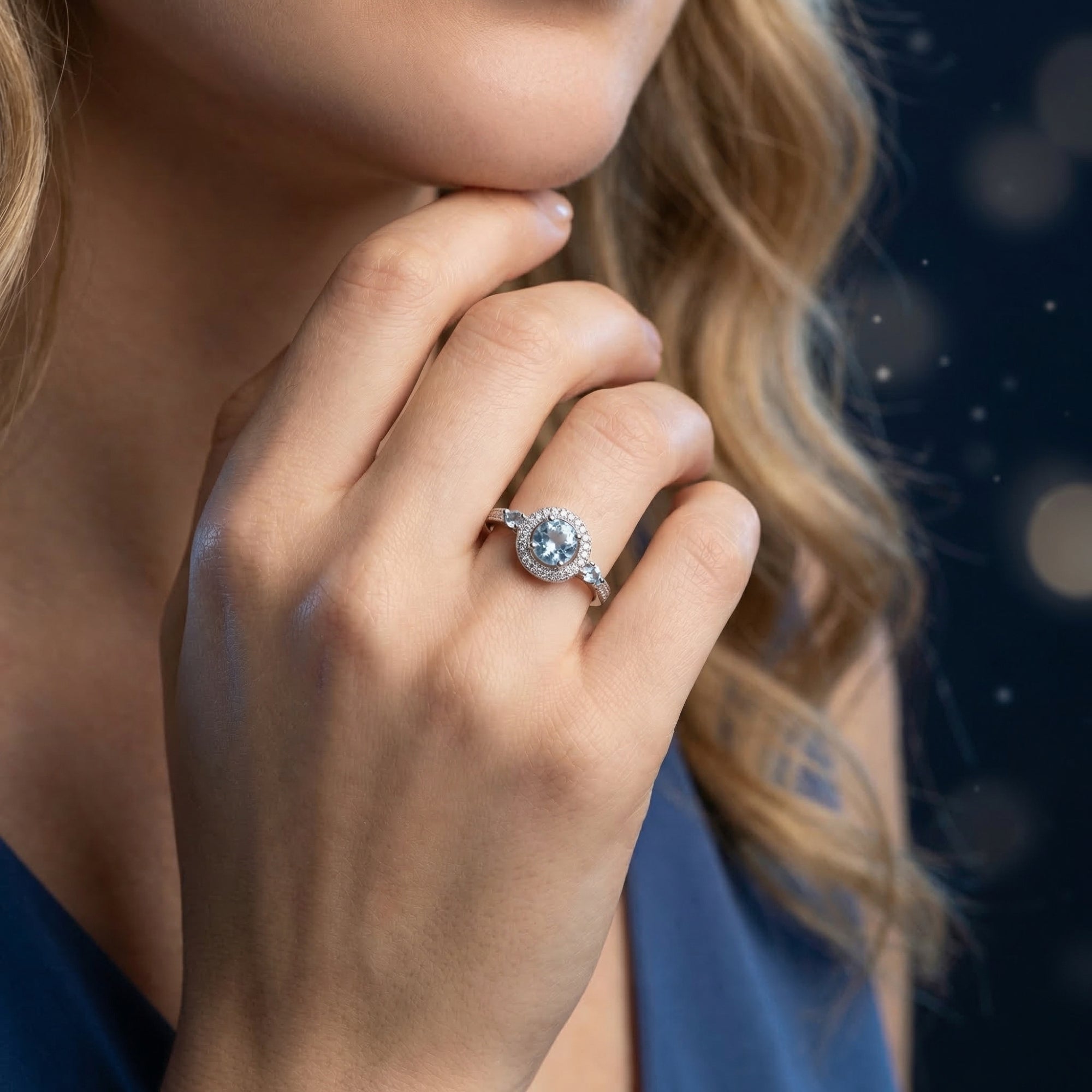 Model wearing the Amabel sterling silver ring with a round blue topaz centerpiece and halo setting.