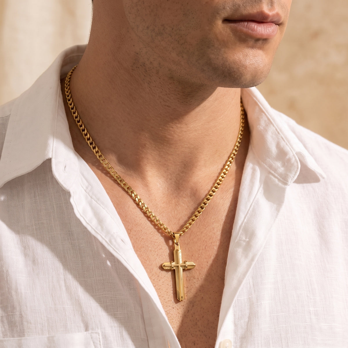 Gold-toned cross pendant and curb chain worn by a model in an open white shirt, shown from a right-facing angle.