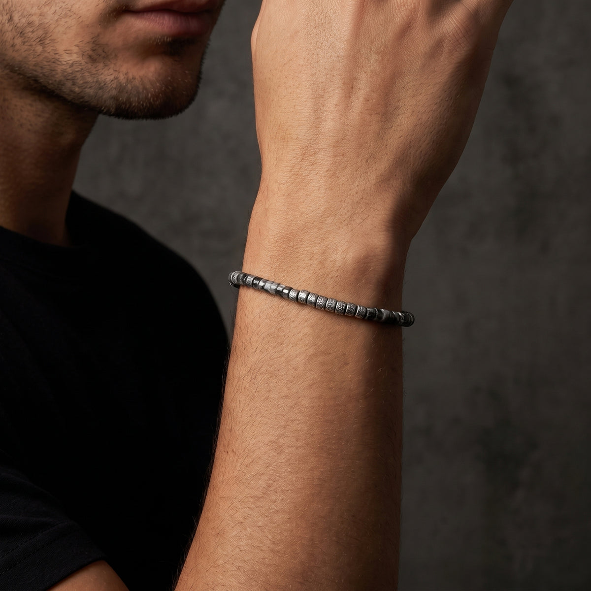 Side view of the silver cylinder bead bracelet worn around a man's forearm against a dark gray background.