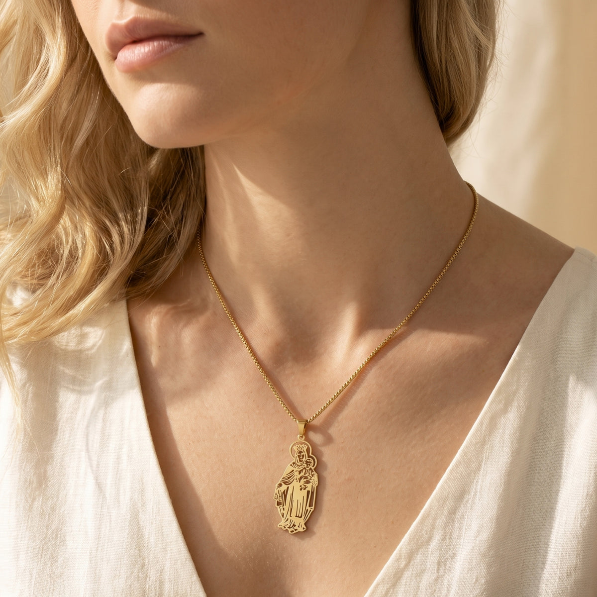 Woman wearing a gold Madonna and Child pendant necklace with a white V-neck top.
